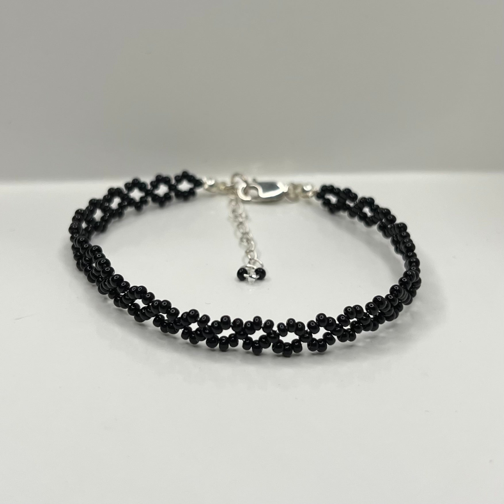 Black beaded bracelet on a white surface with a gray background