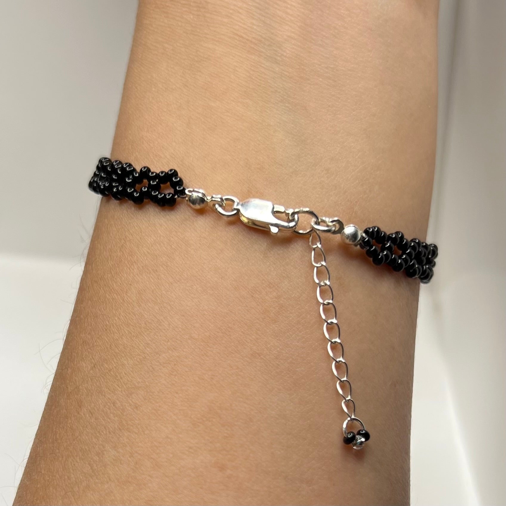Silver bracelet with black beads on a wrist against a white background