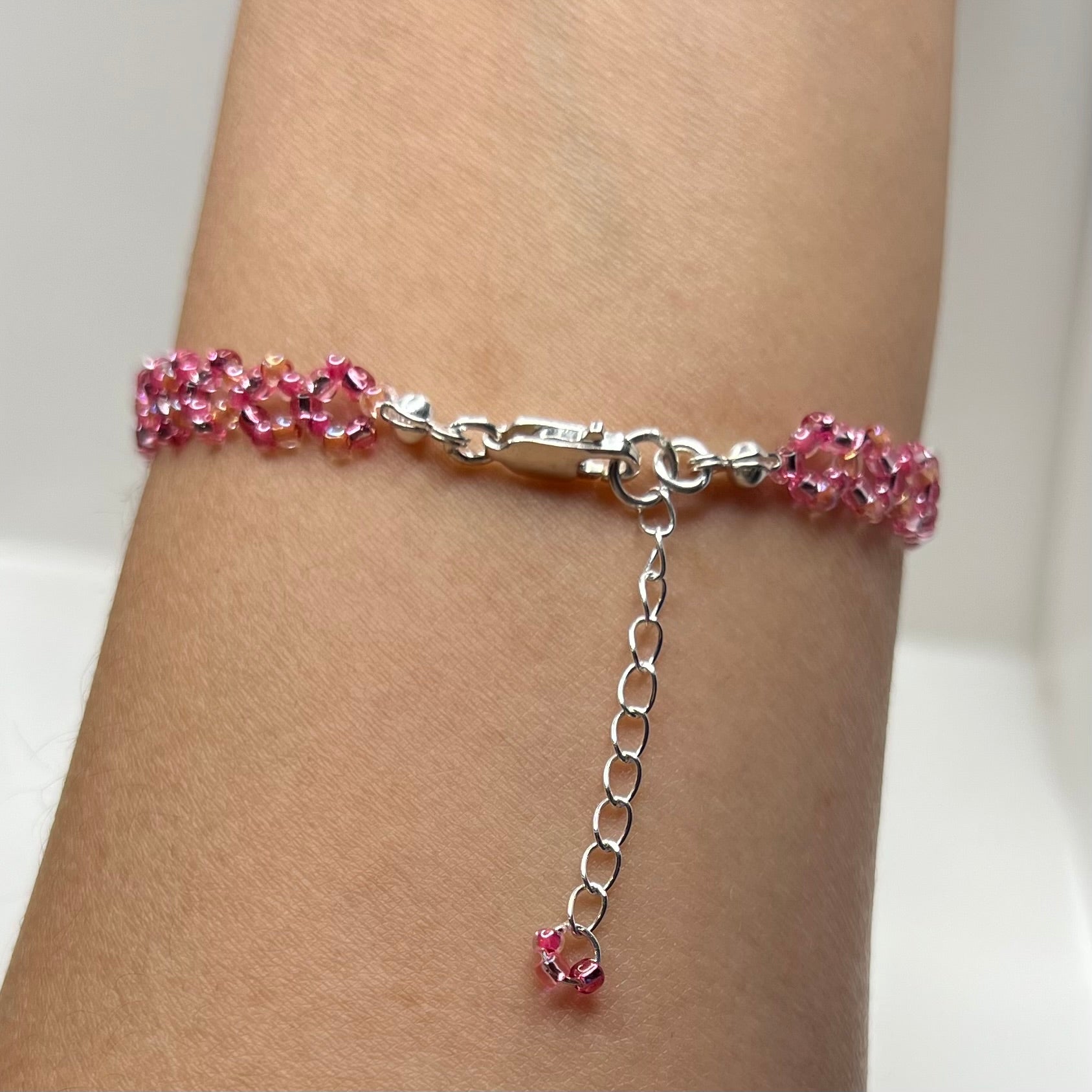 Pink beaded bracelet with a silver chain on a wrist against a white background