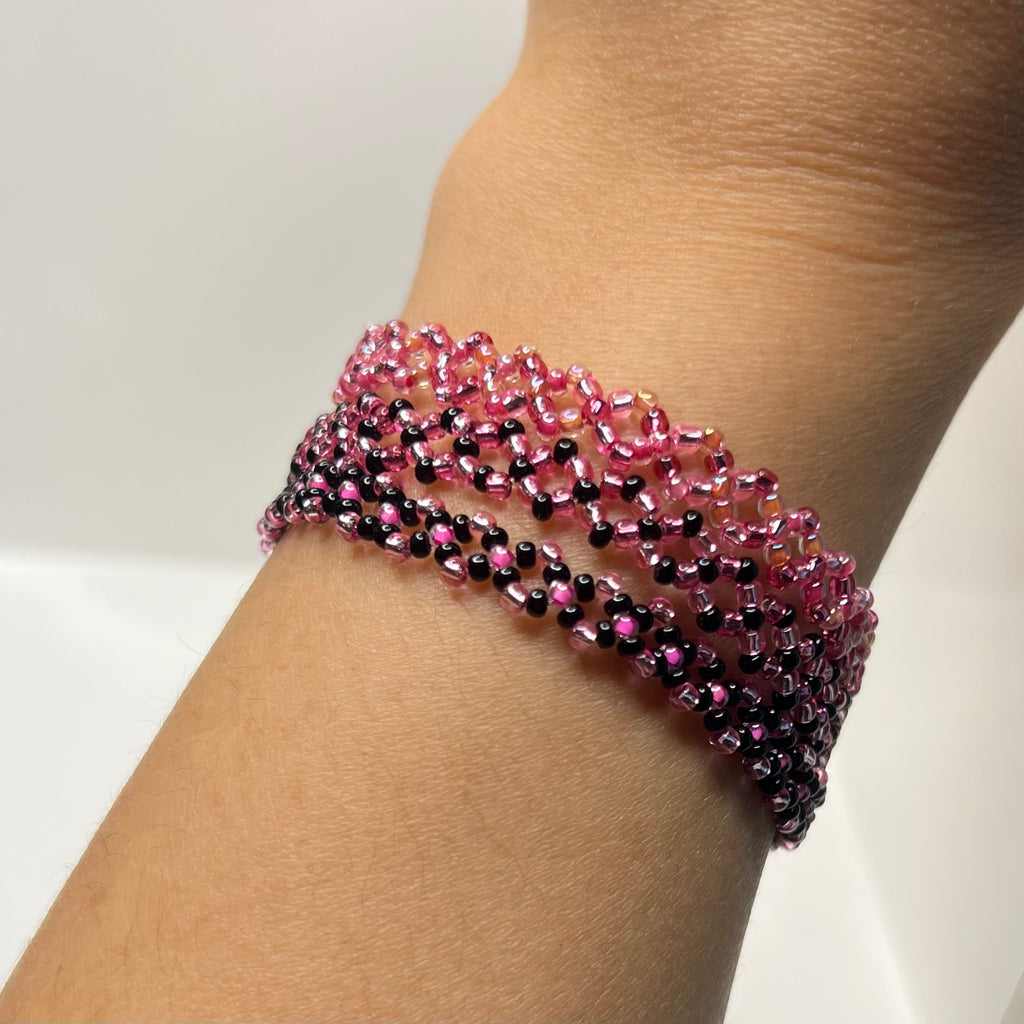 Beaded bracelet with pink and black beads on a wrist against a neutral background