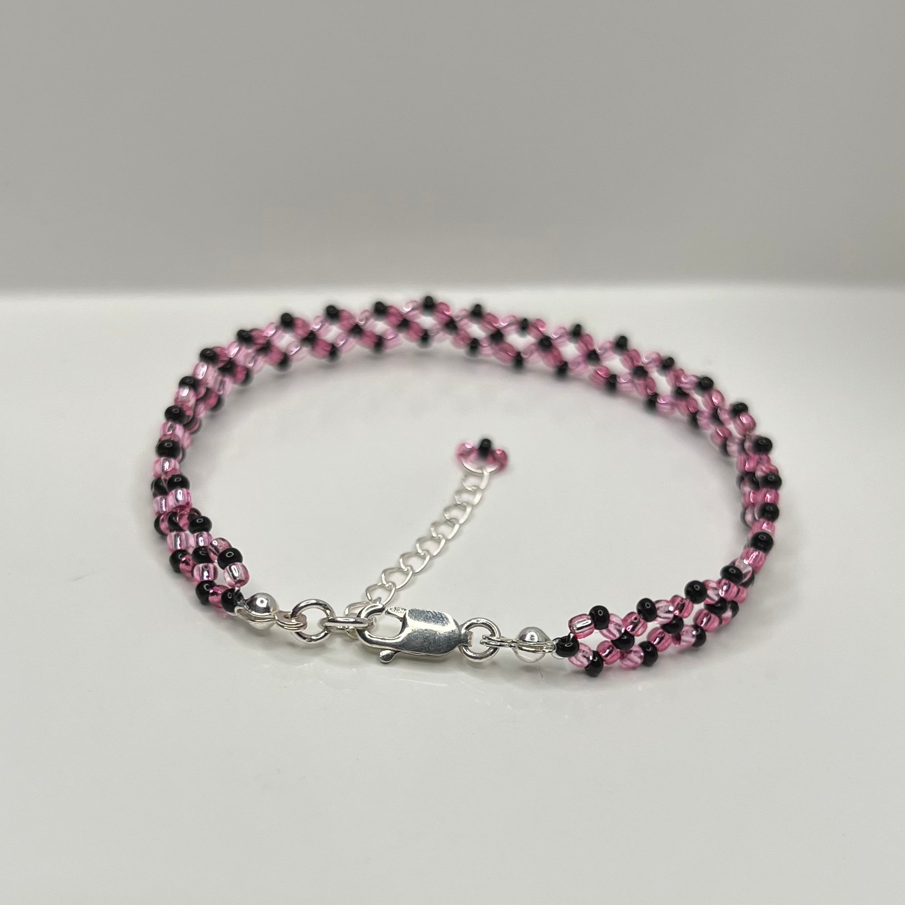 Beaded bracelet with pink and black beads on a silver clasp against a gray background