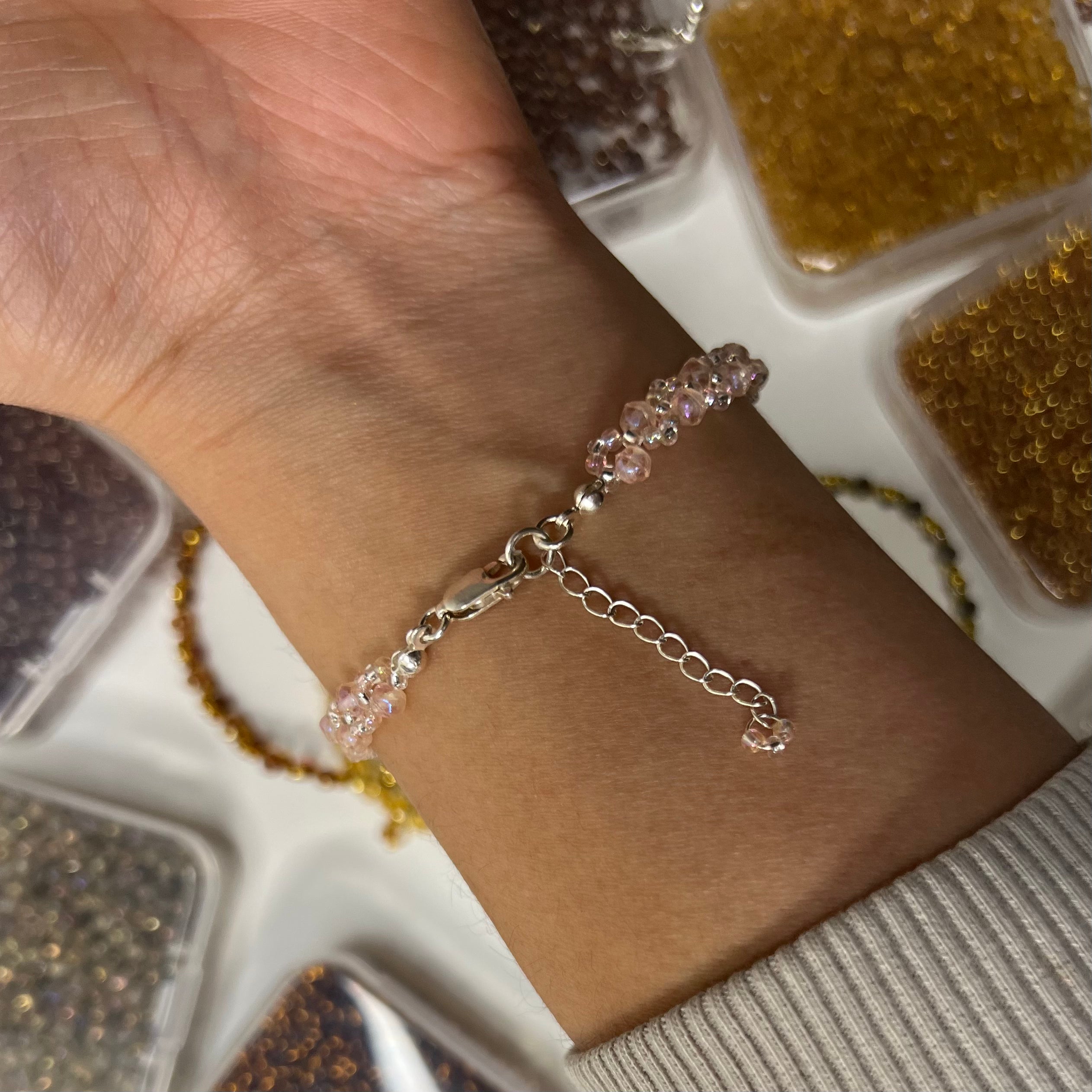 Bracelet on a wrist with a background of small containers filled with beads.