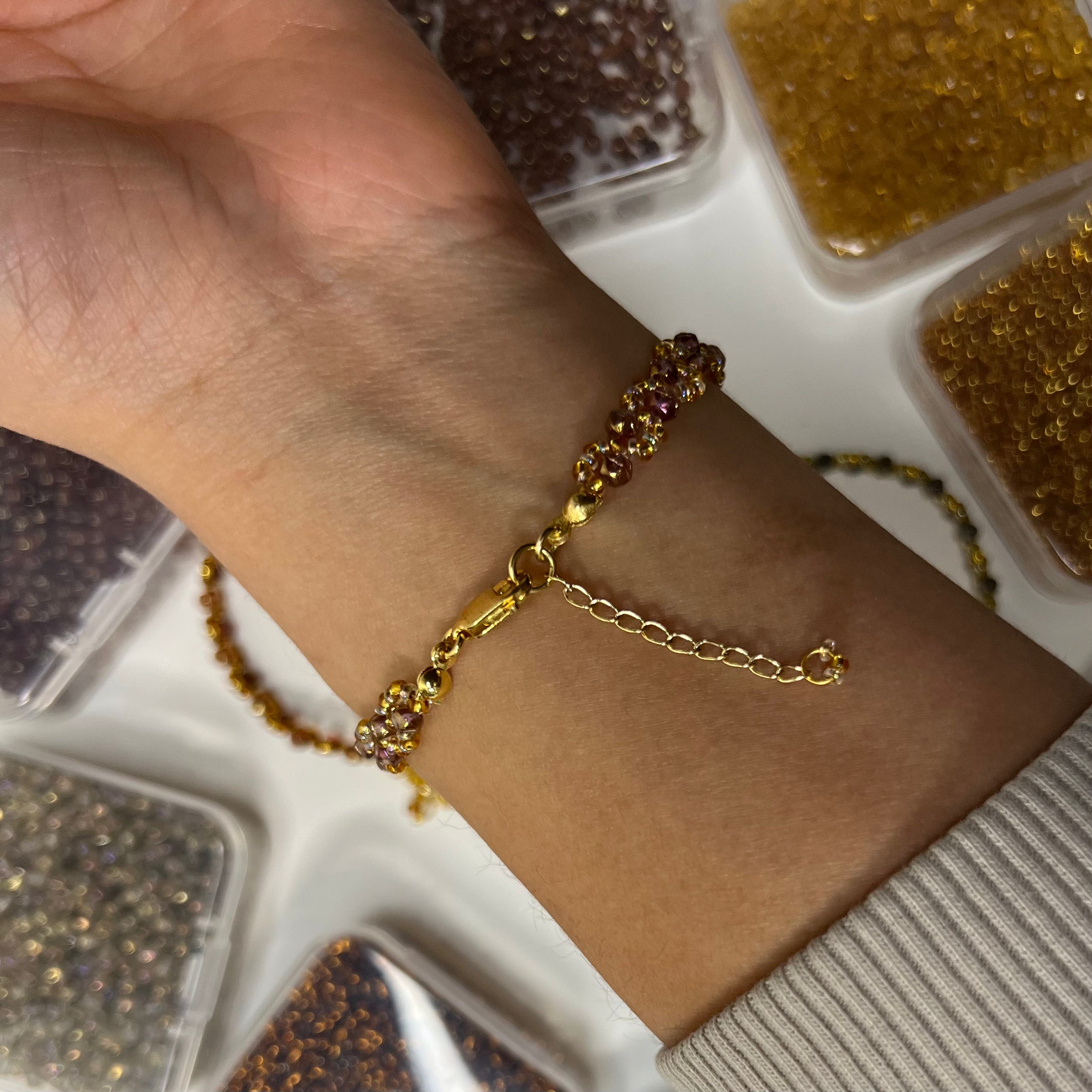 Gold chain bracelet on a wrist with a blurred background of jewelry trays.