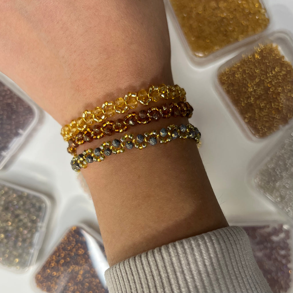 Close-up of a wrist wearing three gold bracelets with a container of beads in the background.