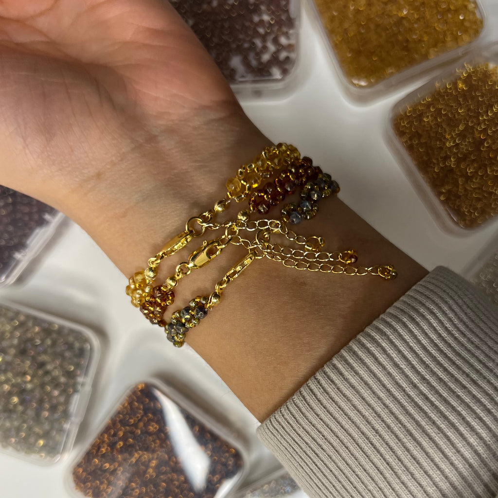 Close-up of a wrist wearing three gold bracelets with a container of beads in the background.