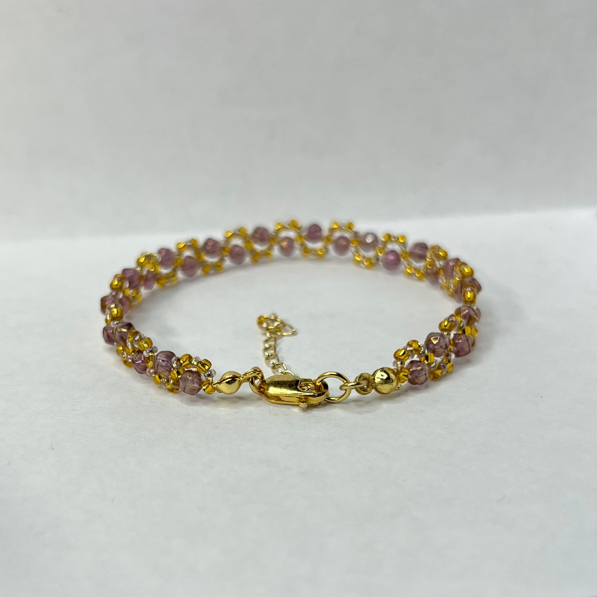 Gold bracelet with purple beads on a white background
