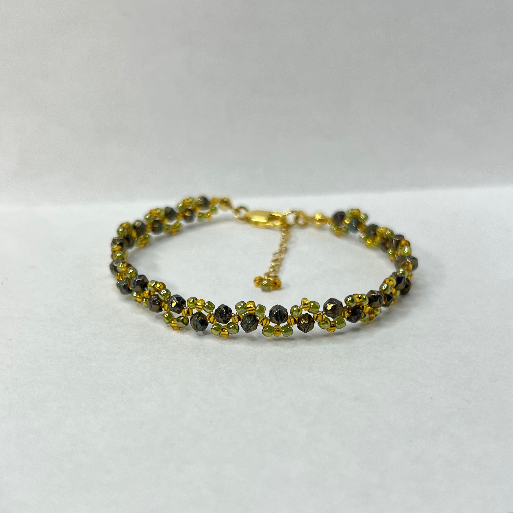 Gold and very dark green beaded bracelet on a white background