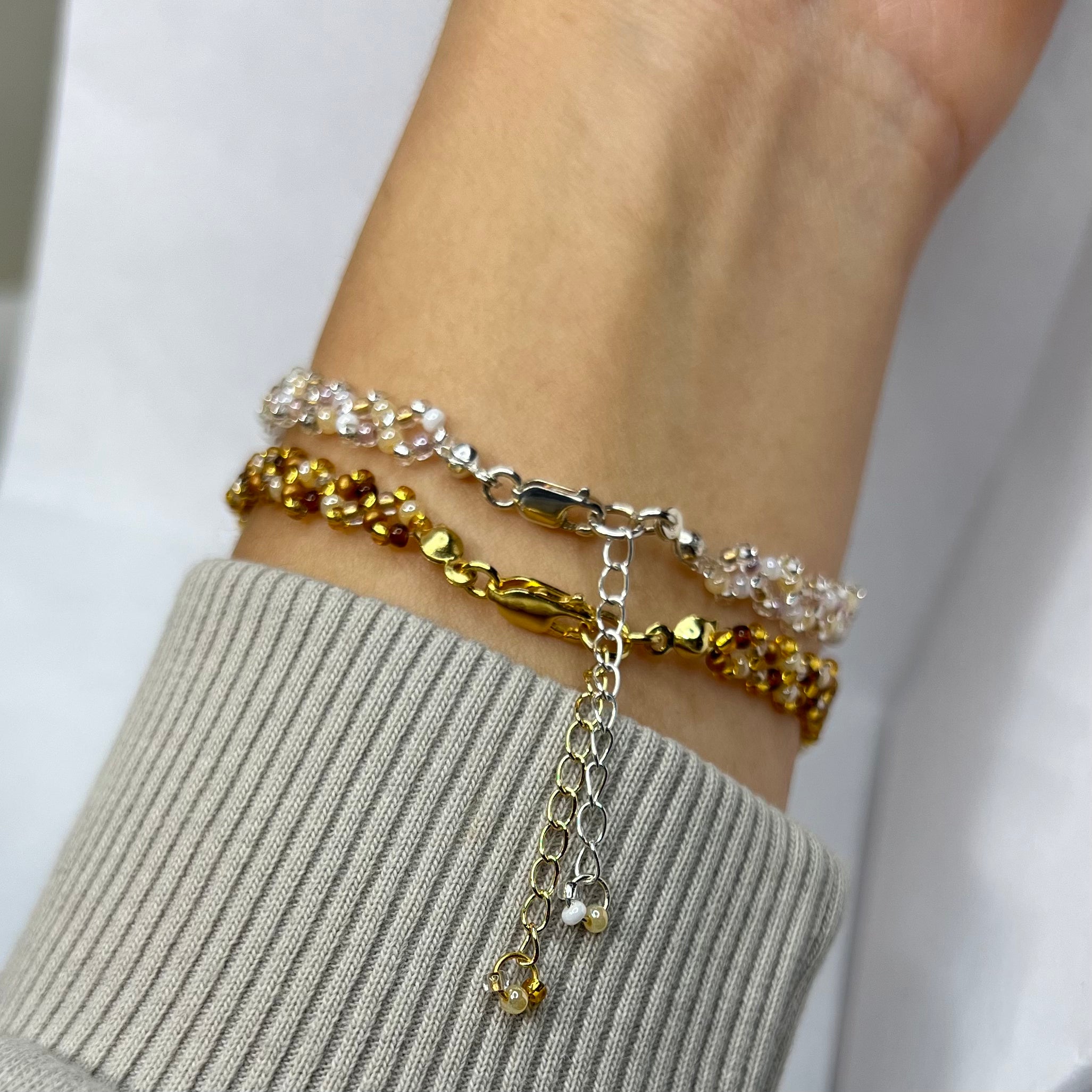 Close-up of a wrist wearing two gold bracelets on a neutral background