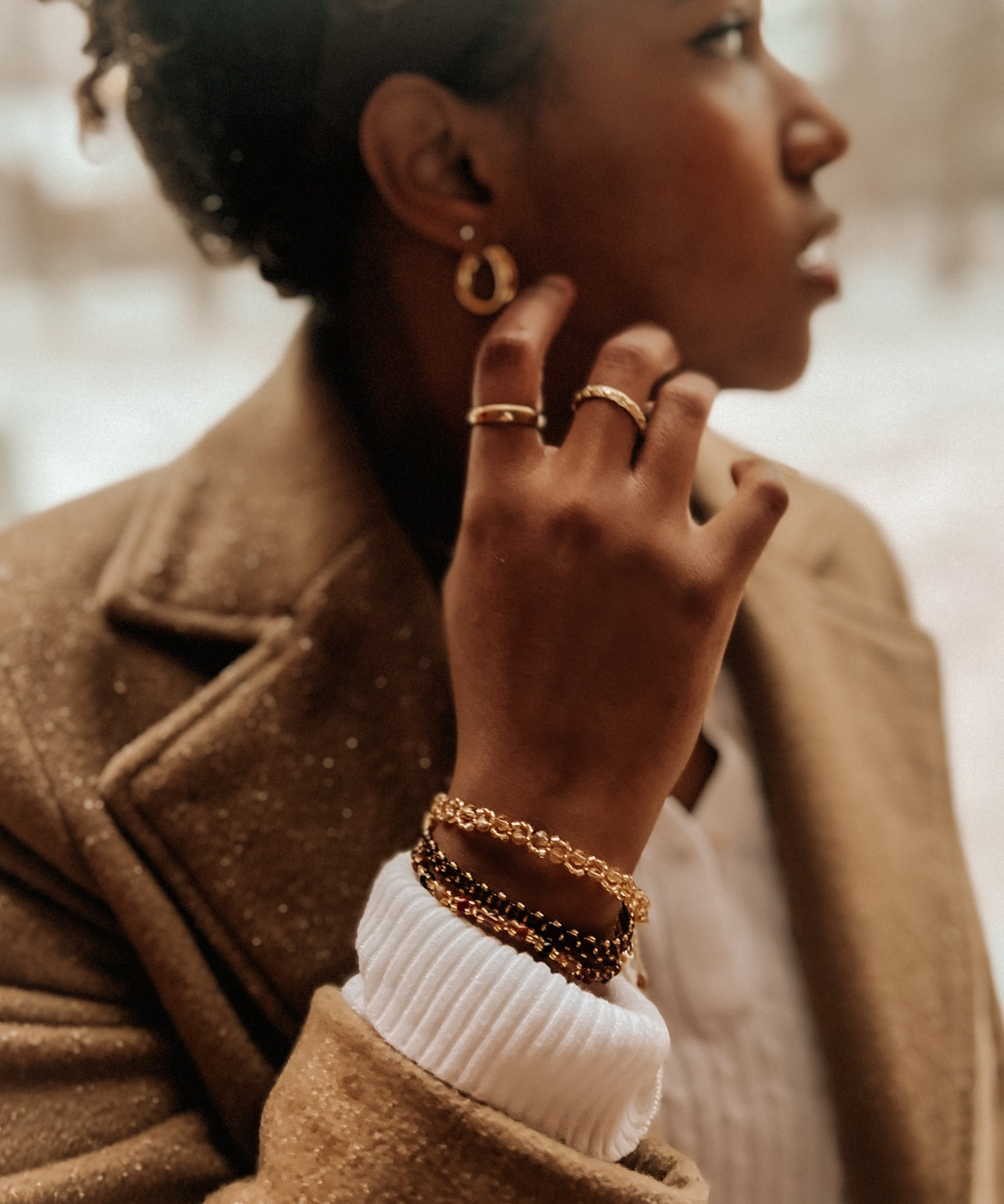 Woman wearing gold jewelry including earrings, rings, and bracelets, with a blurred background.