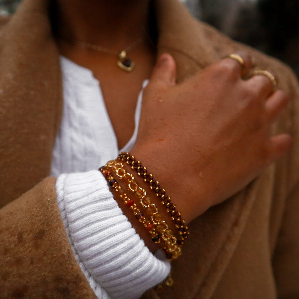 Close-up of a person wearing gold bracelets and rings with a brown coat and white sweater.