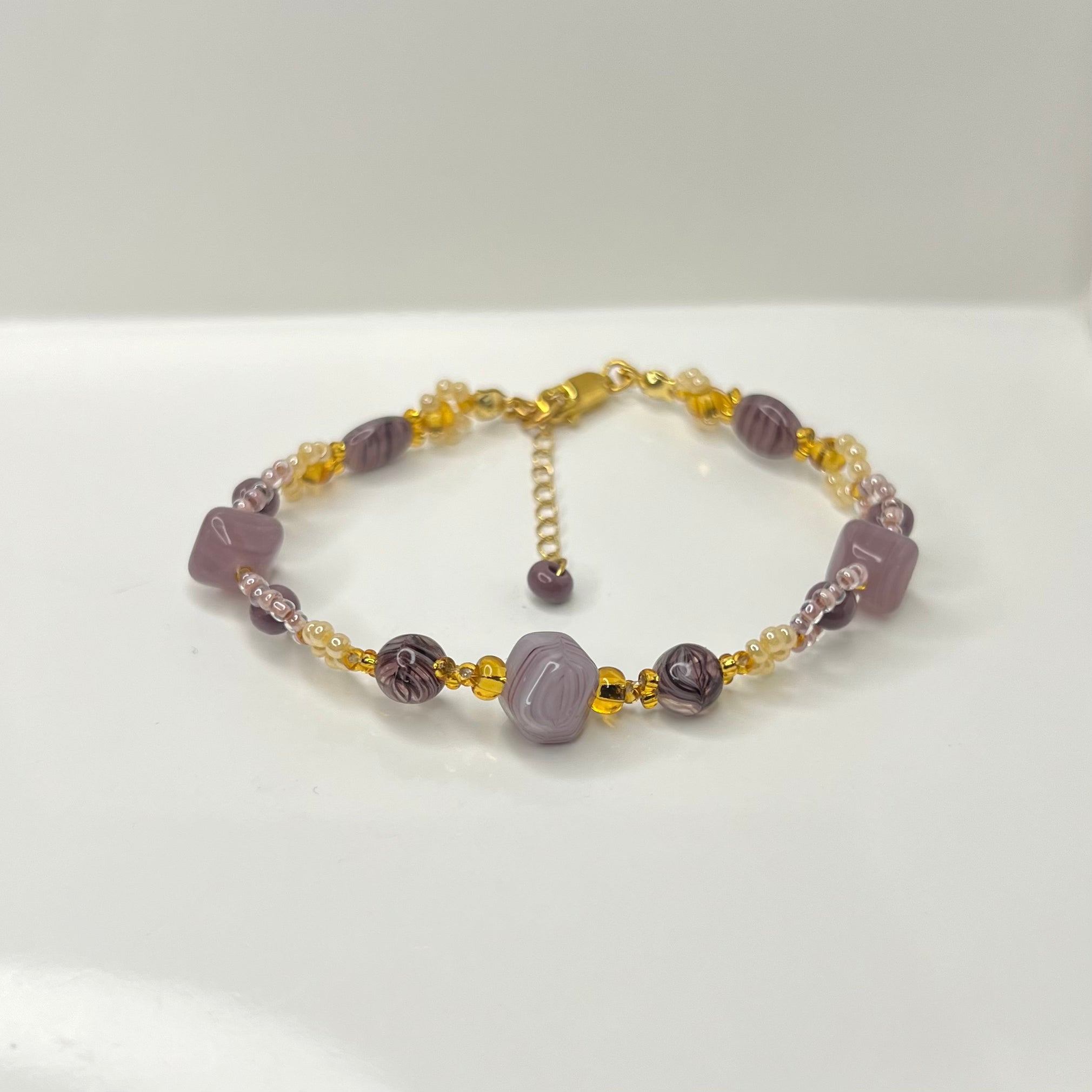 Beaded bracelet with purple and gold beads on a white background