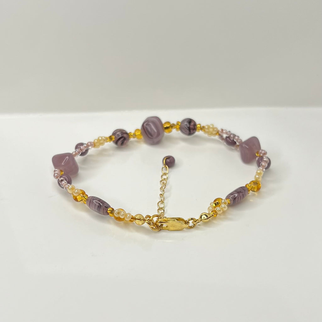 Bracelet with purple beads and gold chain on a white background