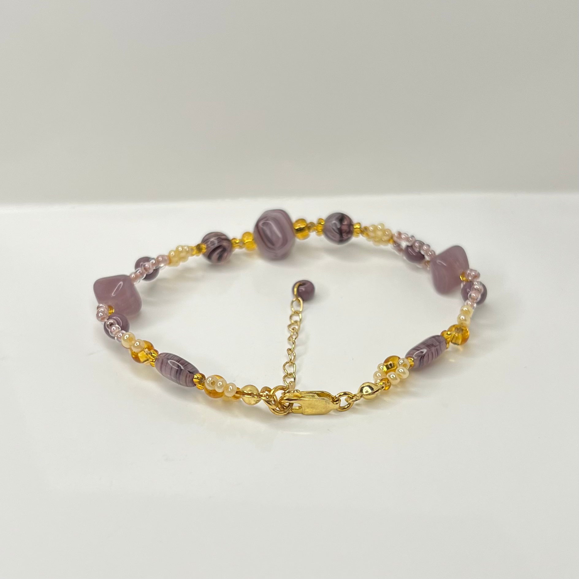 Bracelet with purple beads and gold chain on a white background