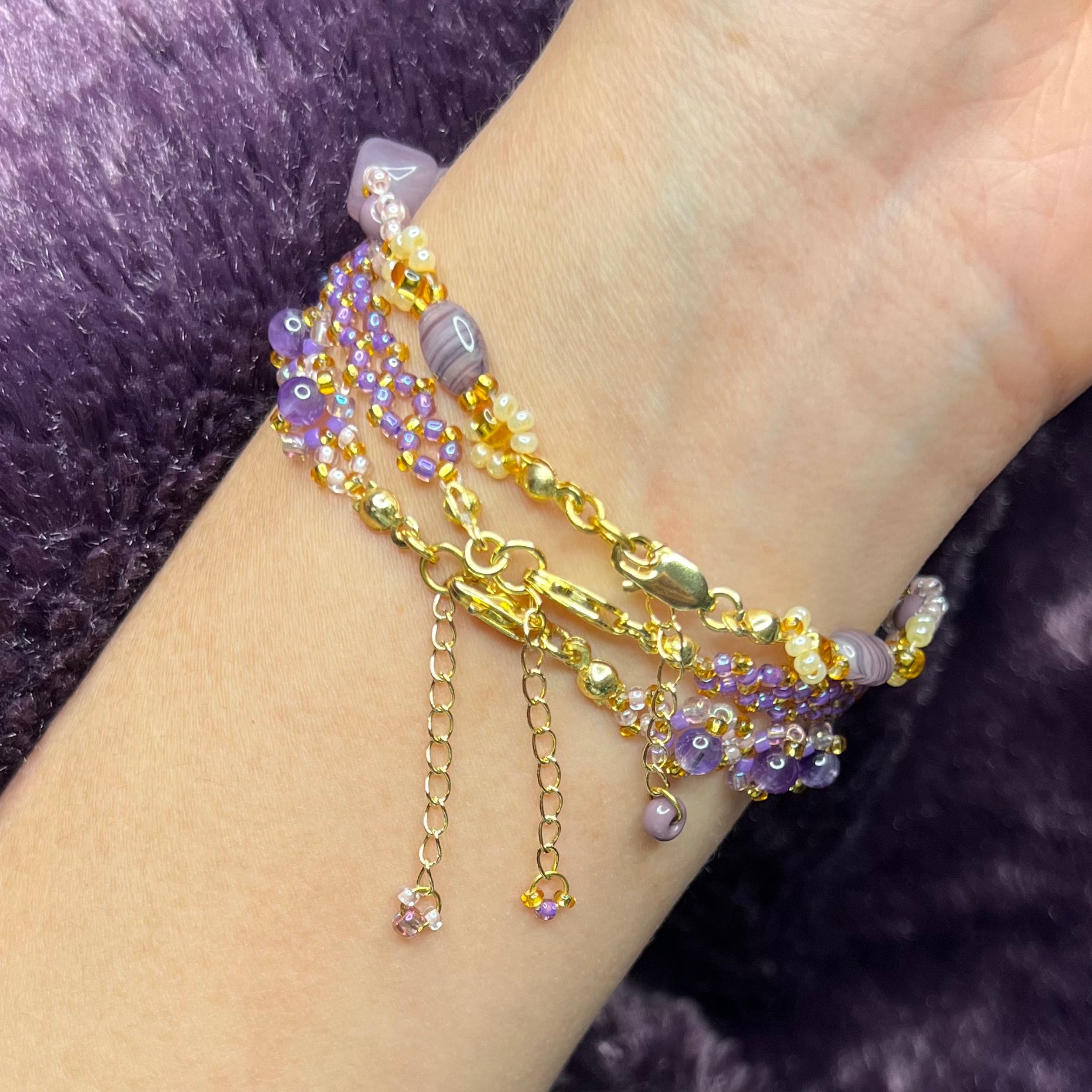 Three bracelets with gold and purple beads on a wrist against a dark background