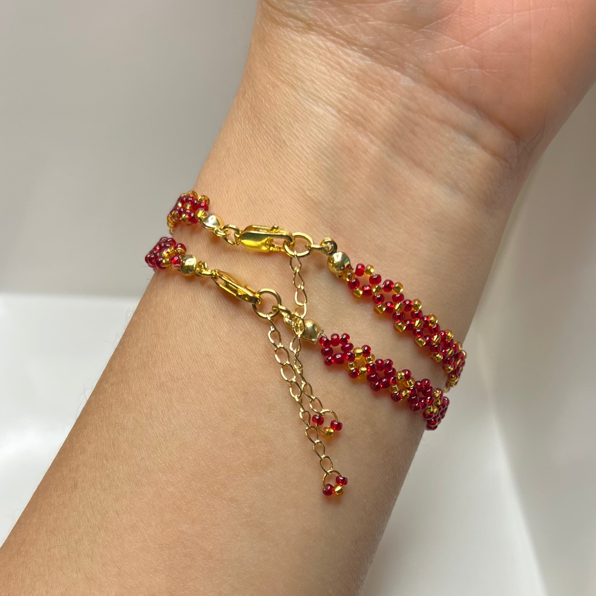 Gold and red beaded bracelet on a wrist against a white background