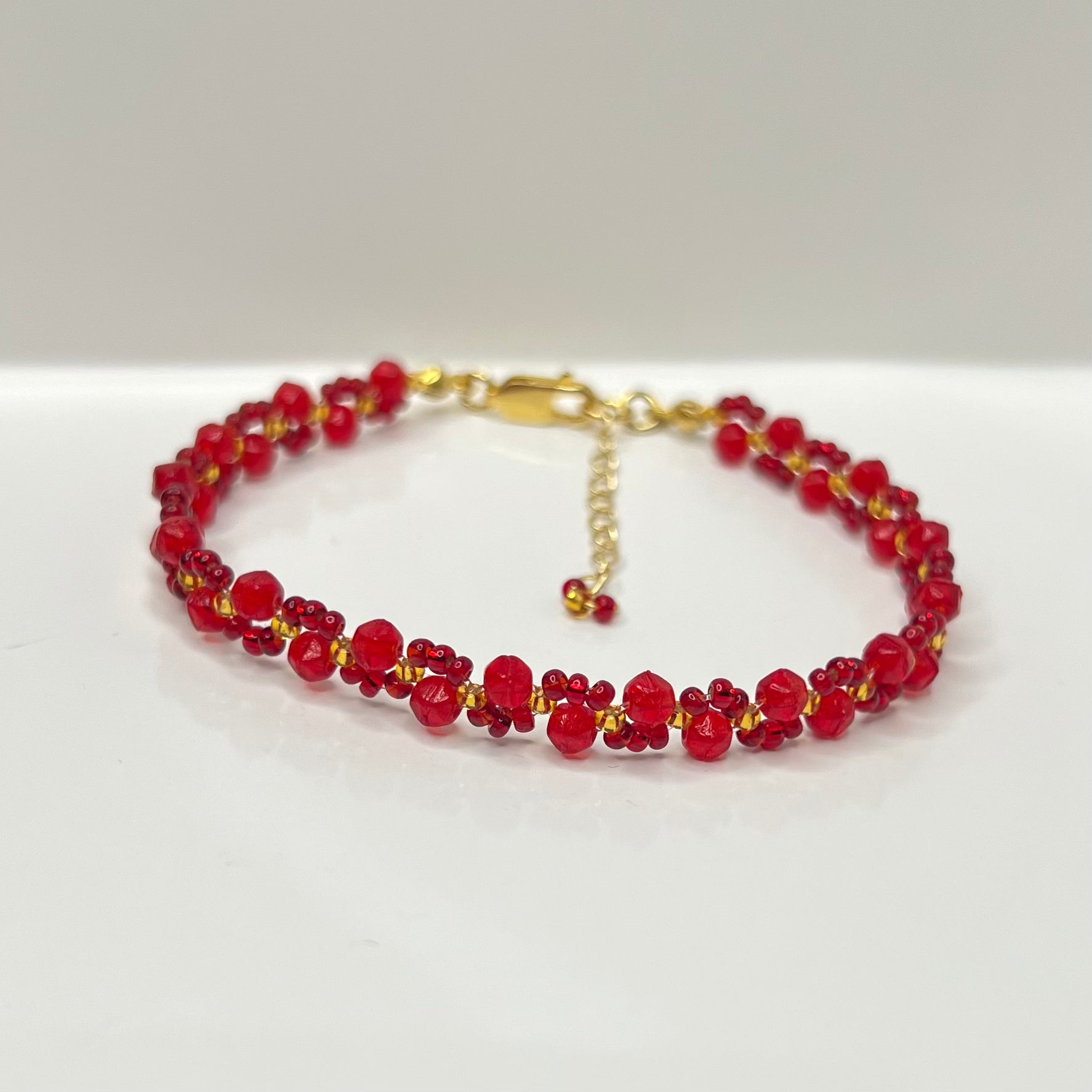 Red beaded bracelet with gold accents on a white background