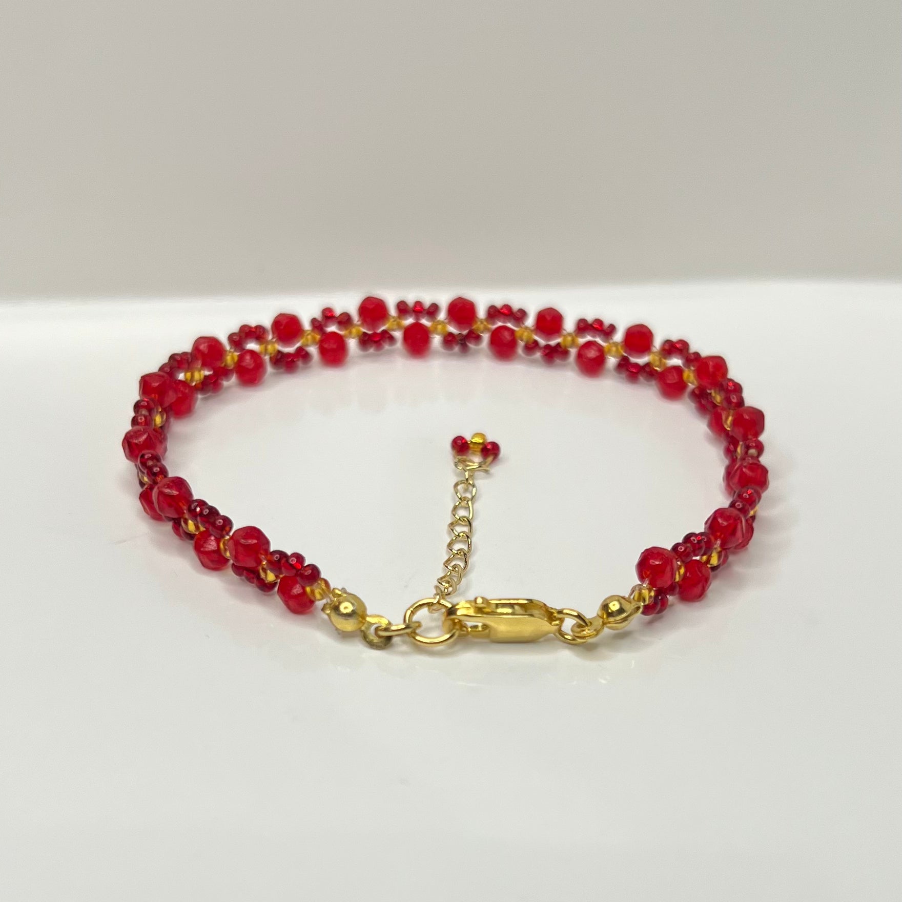 Red beaded bracelet with gold clasp on a white background
