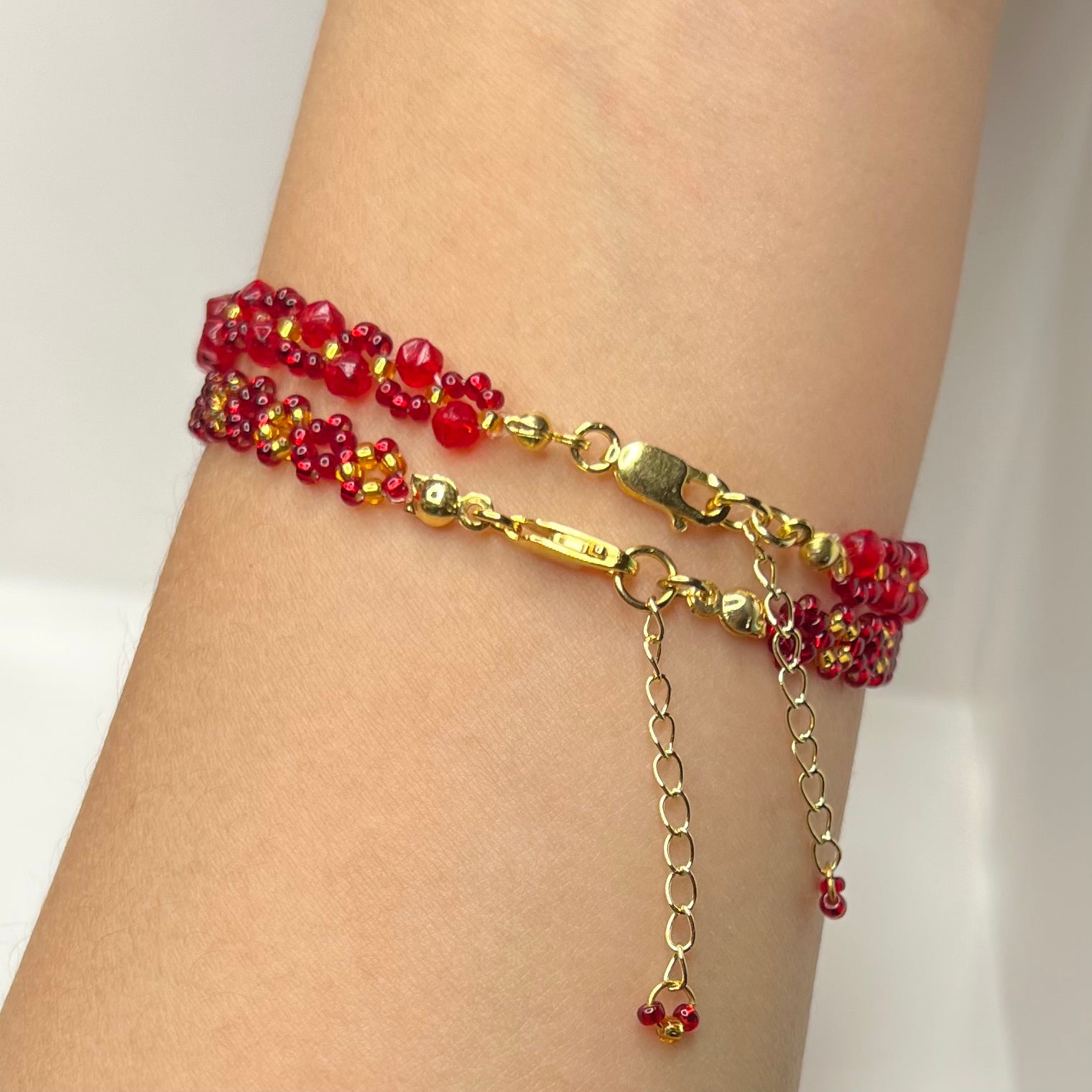 Gold bracelet with red beads on a wrist against a white background