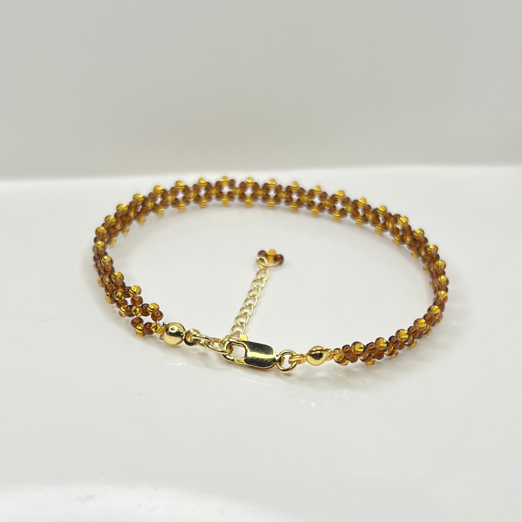 Brown and gold beaded bracelet with a chain on a white background