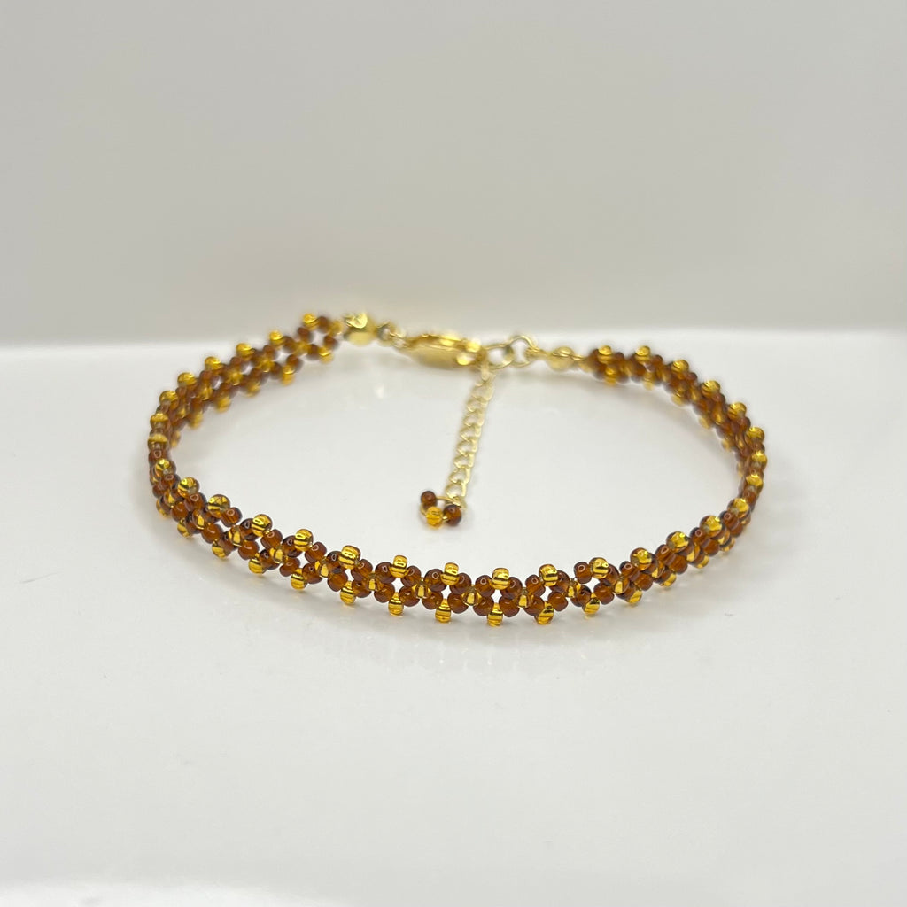 Gold bracelet with small brown and gold beads on a white background