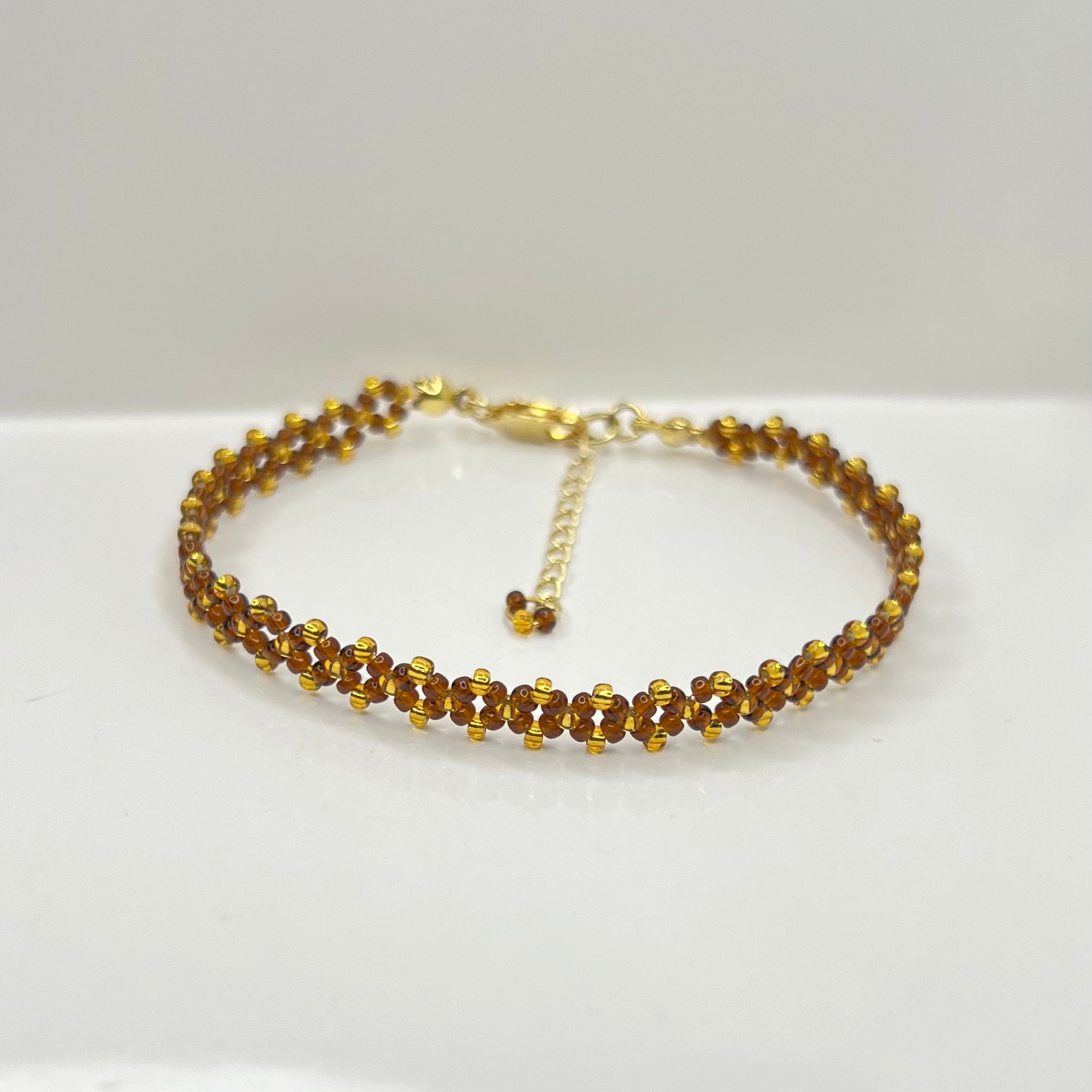 Gold bracelet with small brown and gold beads on a white background