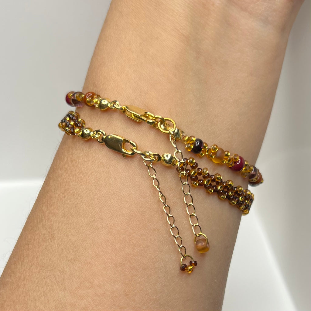Gold chain bracelet with red and gold beads on a wrist against a white background