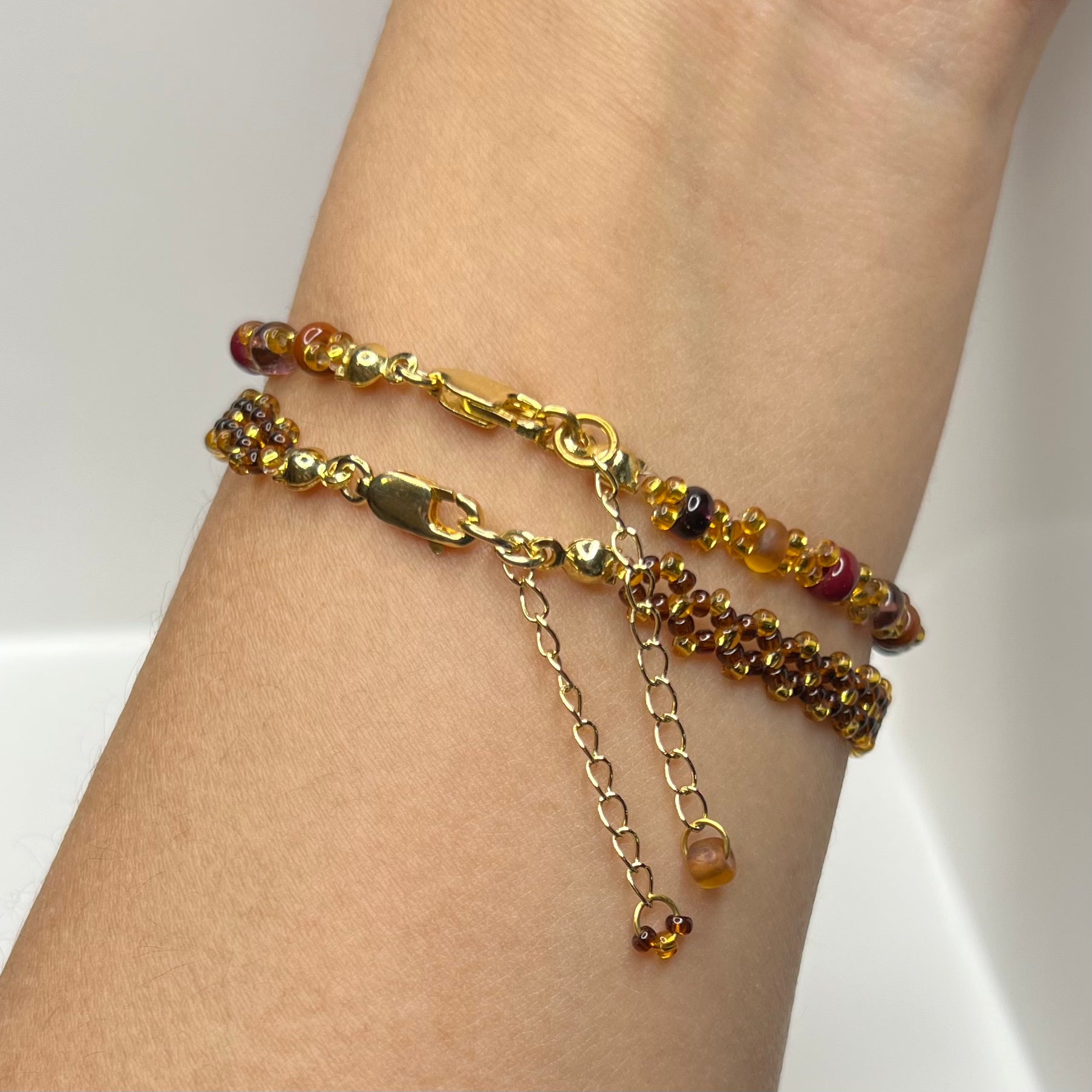 Gold chain bracelet with red and gold beads on a wrist against a white background