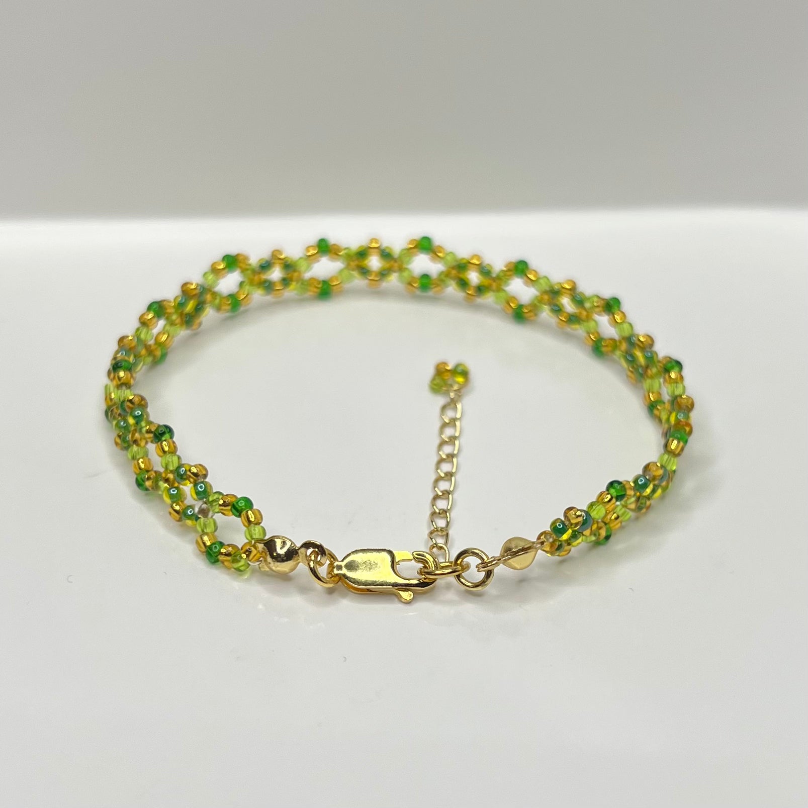 Green beaded bracelet with gold clasp on a white background