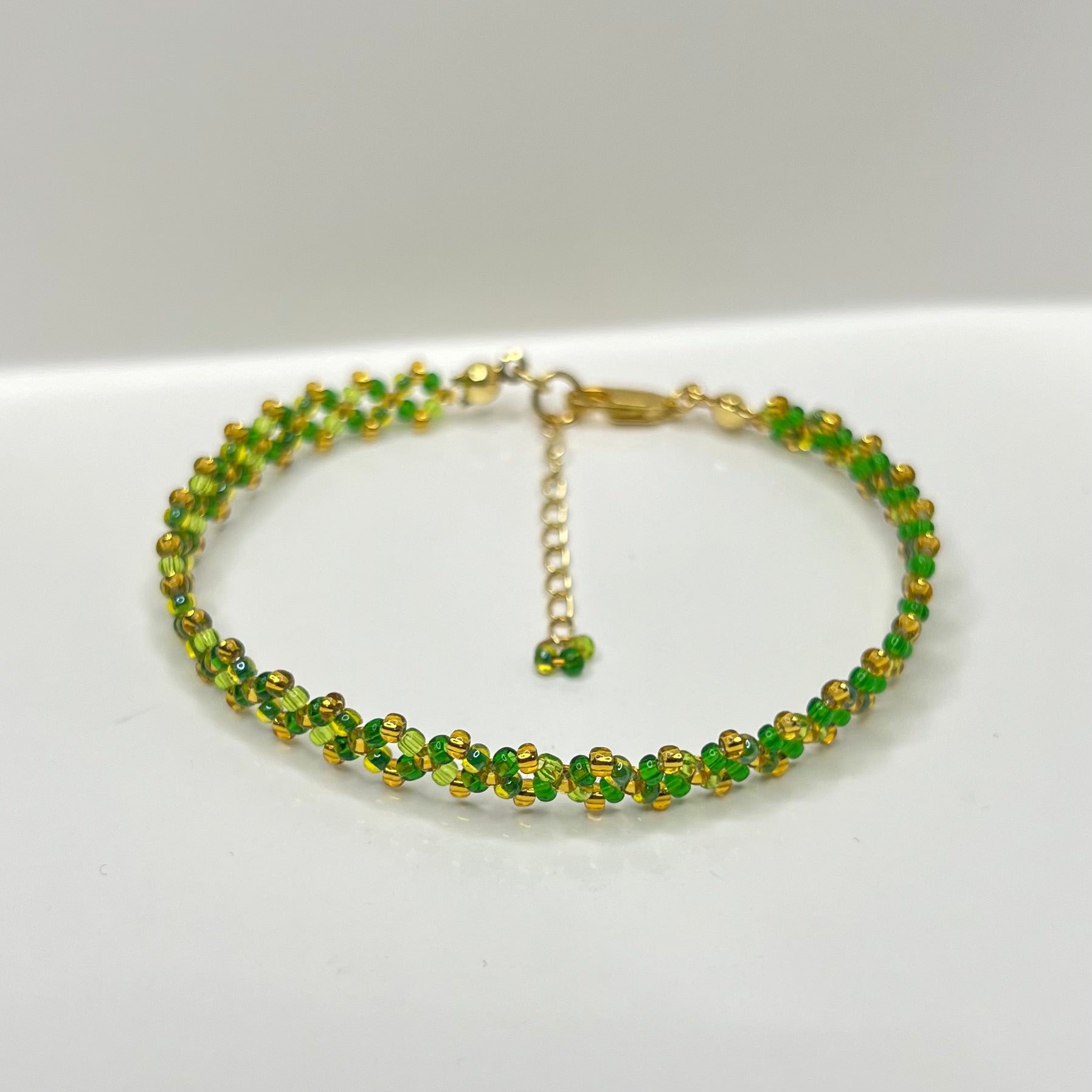 Green beaded bracelet with gold accents on a white background
