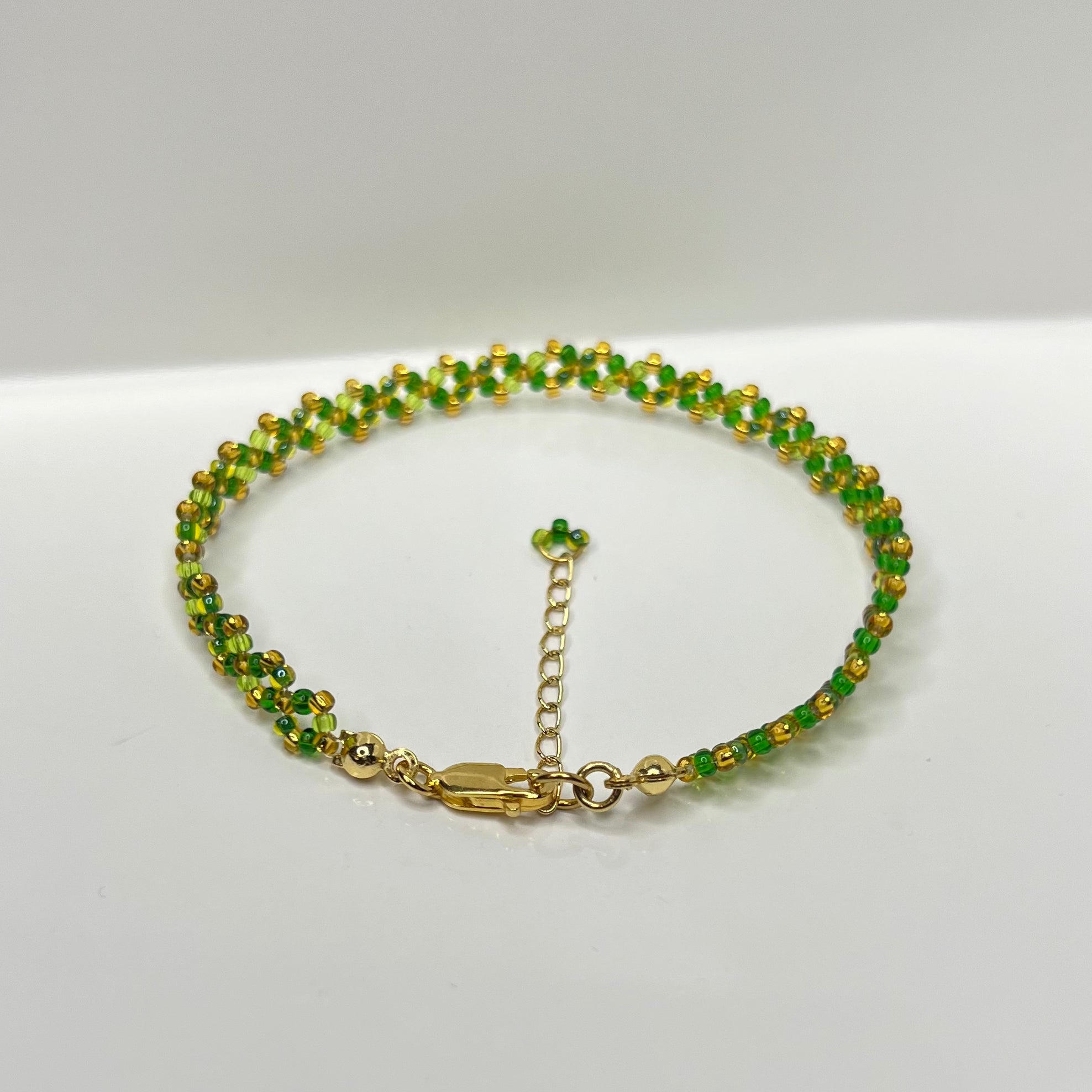 Green beaded bracelet with gold chain on a white background