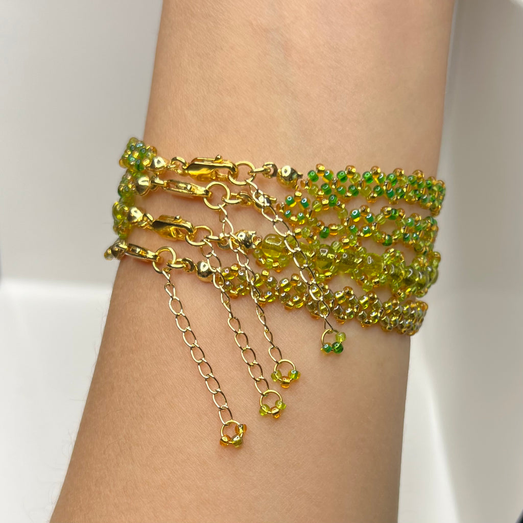 Gold and green beaded bracelets on a wrist against a white background