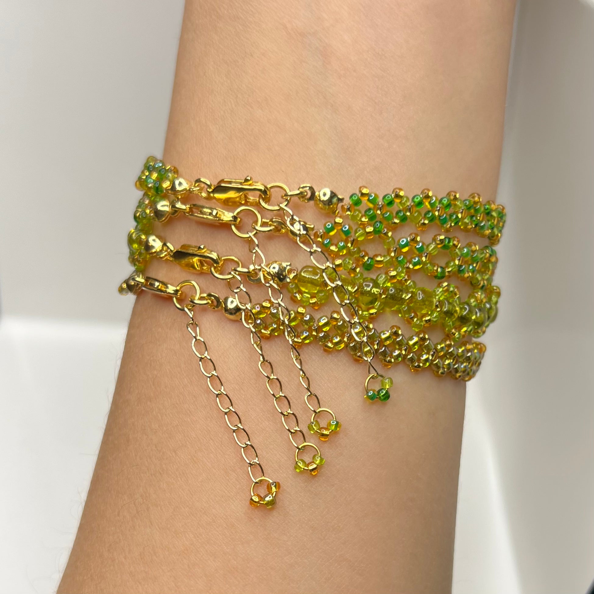 Gold and green beaded bracelets on a wrist against a white background