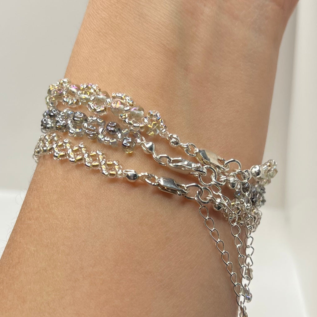 Silver chain bracelets on a person's wrist against a neutral background