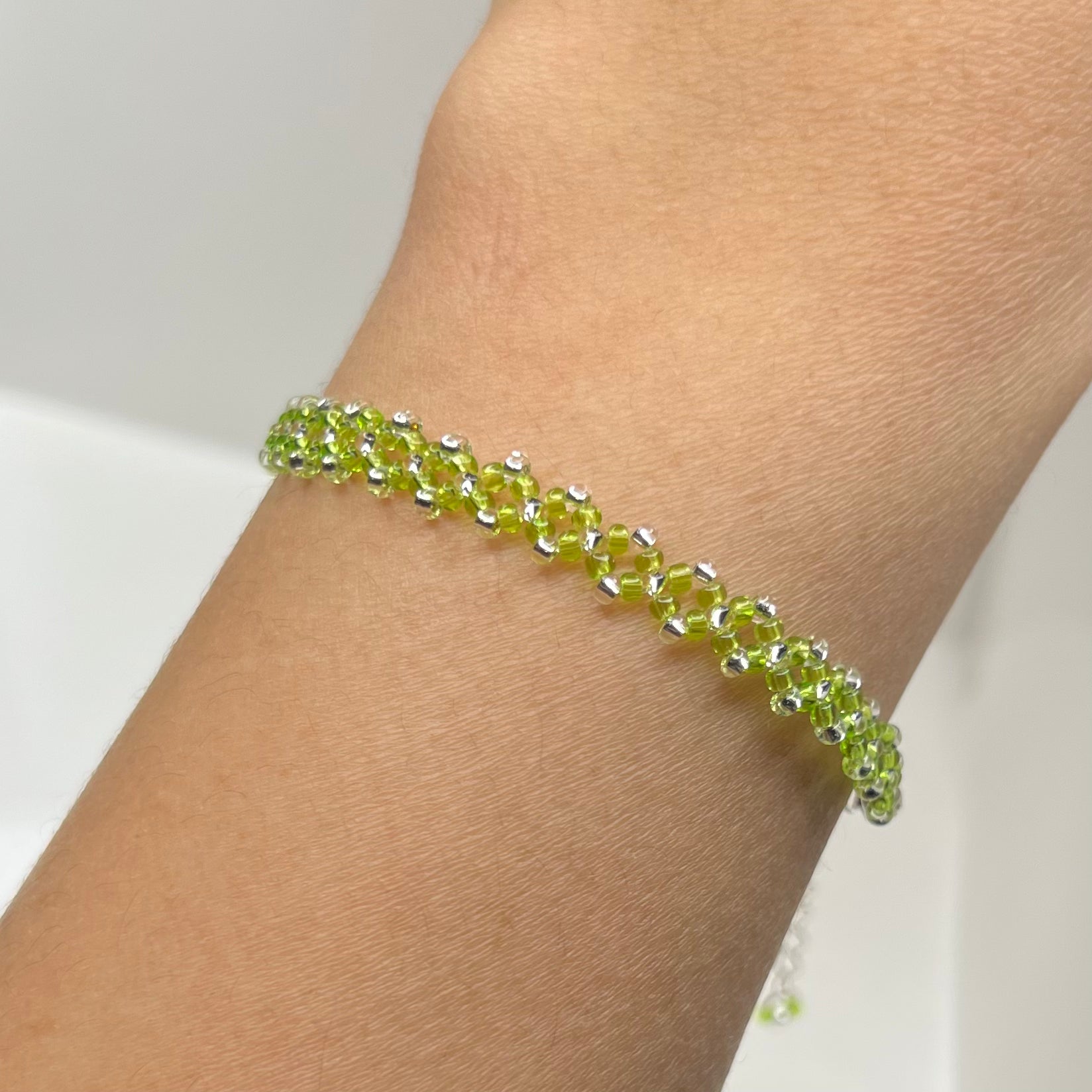 Green beaded bracelet on a wrist with a neutral background