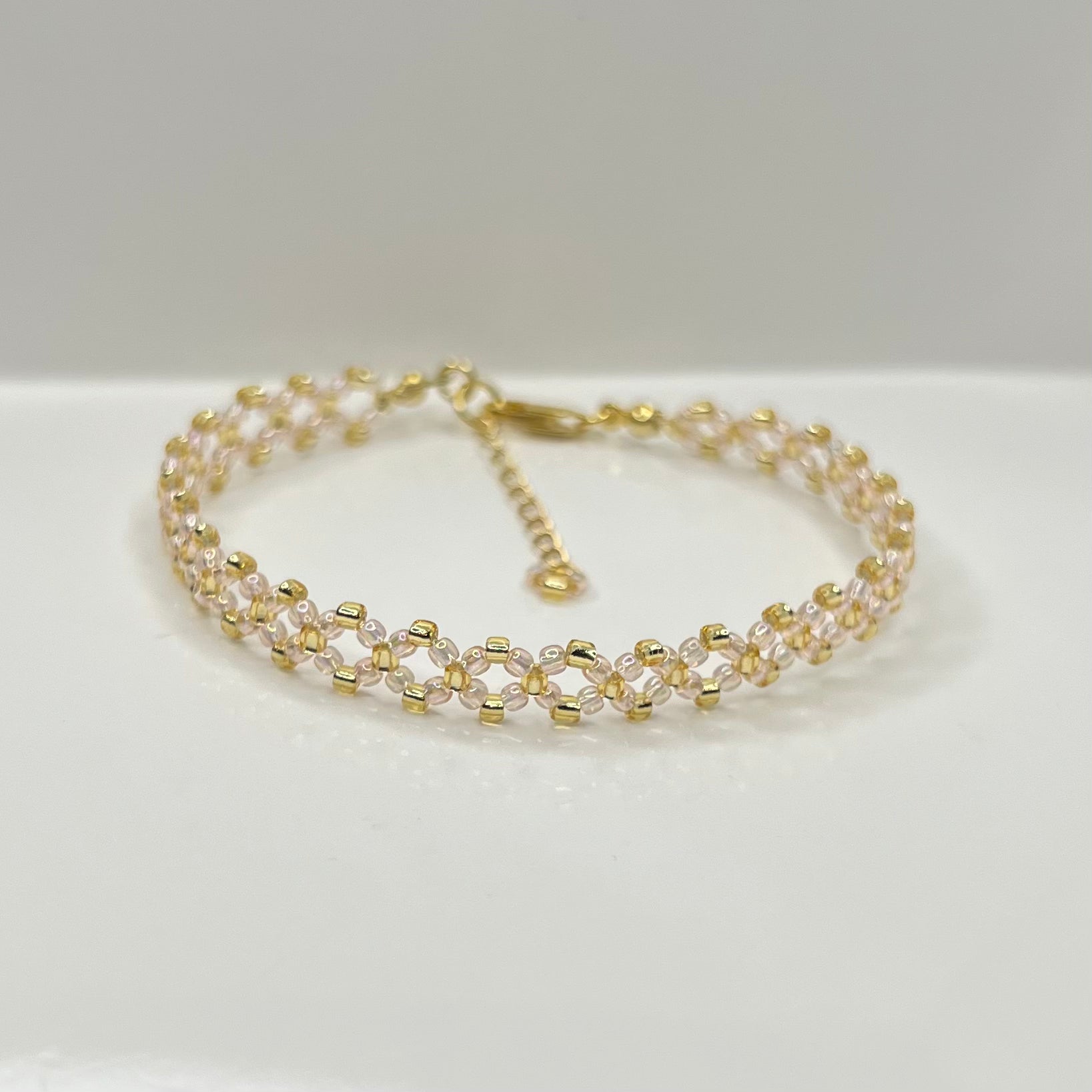 Gold and baby pink beaded bracelet on a white background