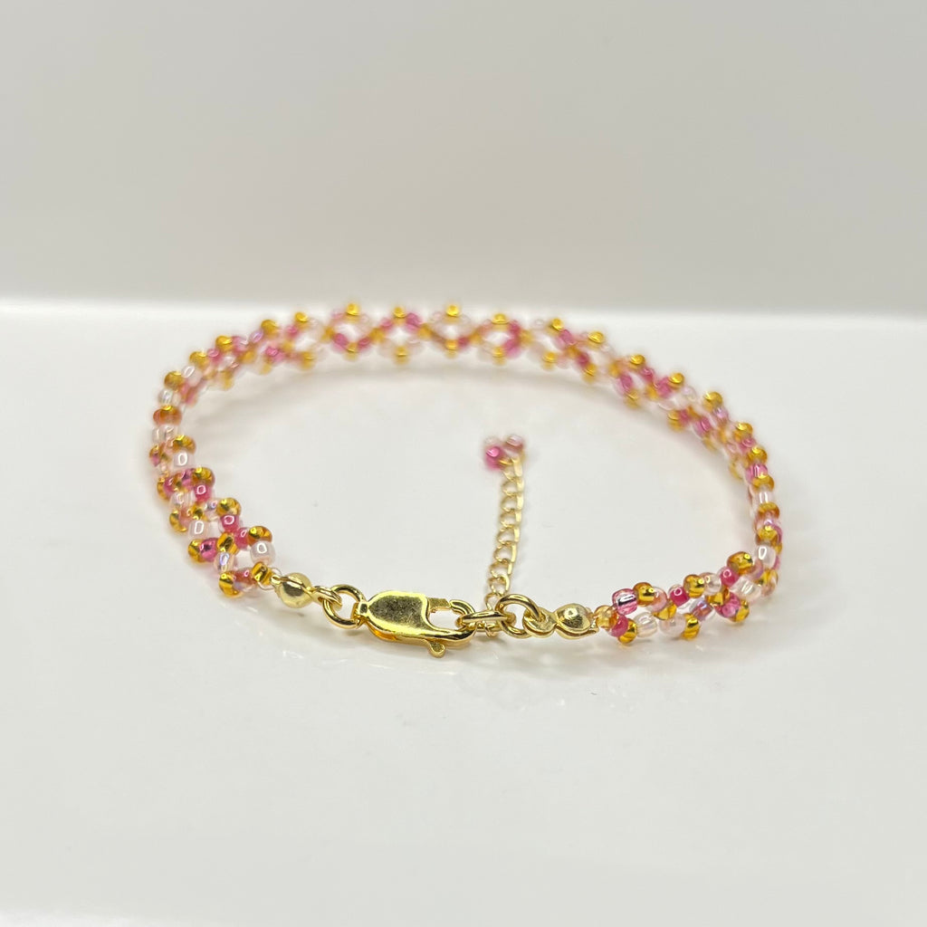 Multicolored pink beaded bracelet with gold clasp on a white background