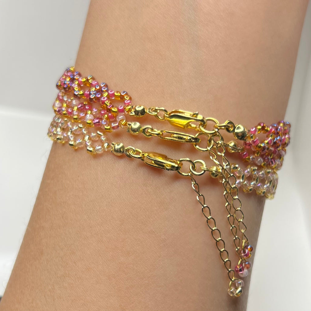 Multicolored beaded bracelet with gold chain on a wrist against a white background